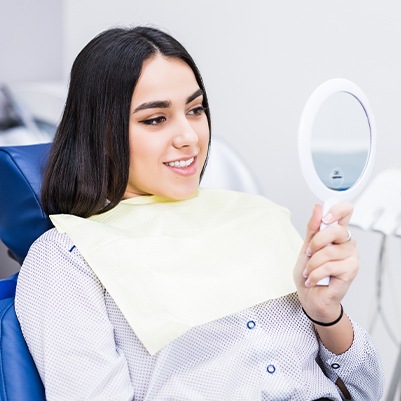 Woman looking at her smile makeover in mirror