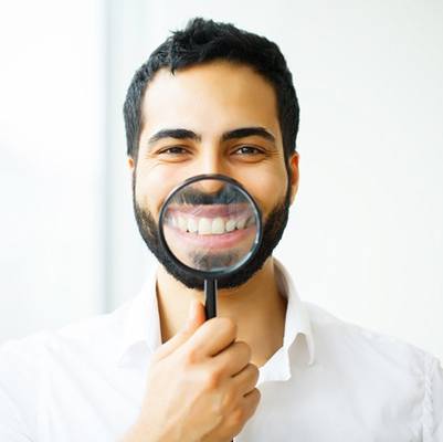 man in white shirt holding magnifying glass to his smile