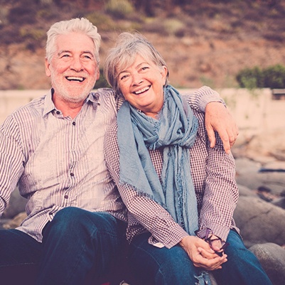 Two seniors sitting at edge of creek and smiling 