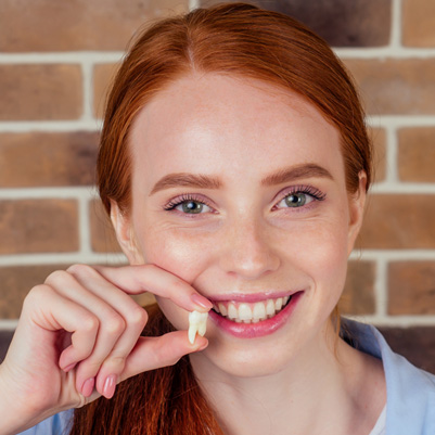 Redhead smiling holding extracted tooth next to her smile
