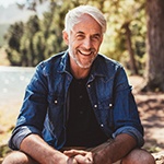 man sitting on a log by a pond 