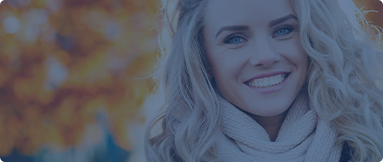 Woman in scarf smiling outdoors among autumn leaves