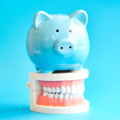Piggy bank atop model teeth representing cost of Invisalign in Friso