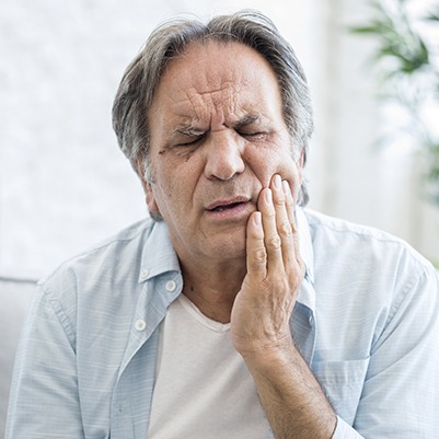 Man in need of TMJ therapy holding jaw