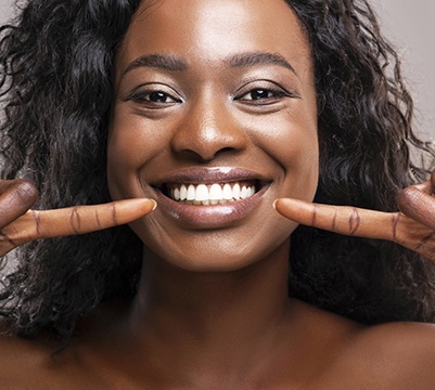 Woman with white teeth pointing to her smile