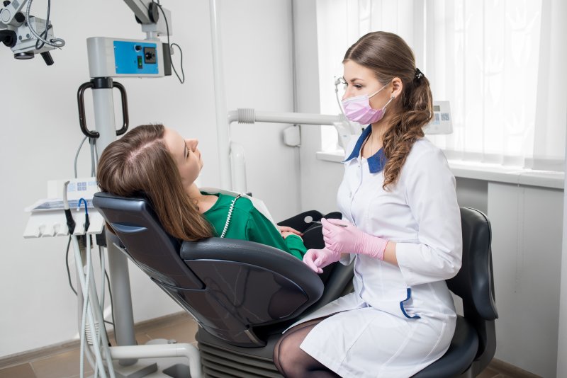 a young woman sitting in a dentist’s chair while an emergency dentist prepares to examine the patient