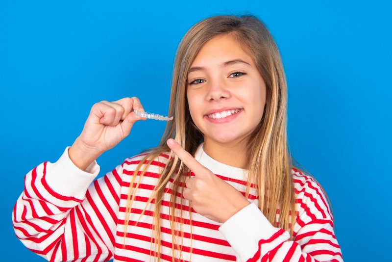 A girl smiling and pointing at the clear aligner she took off