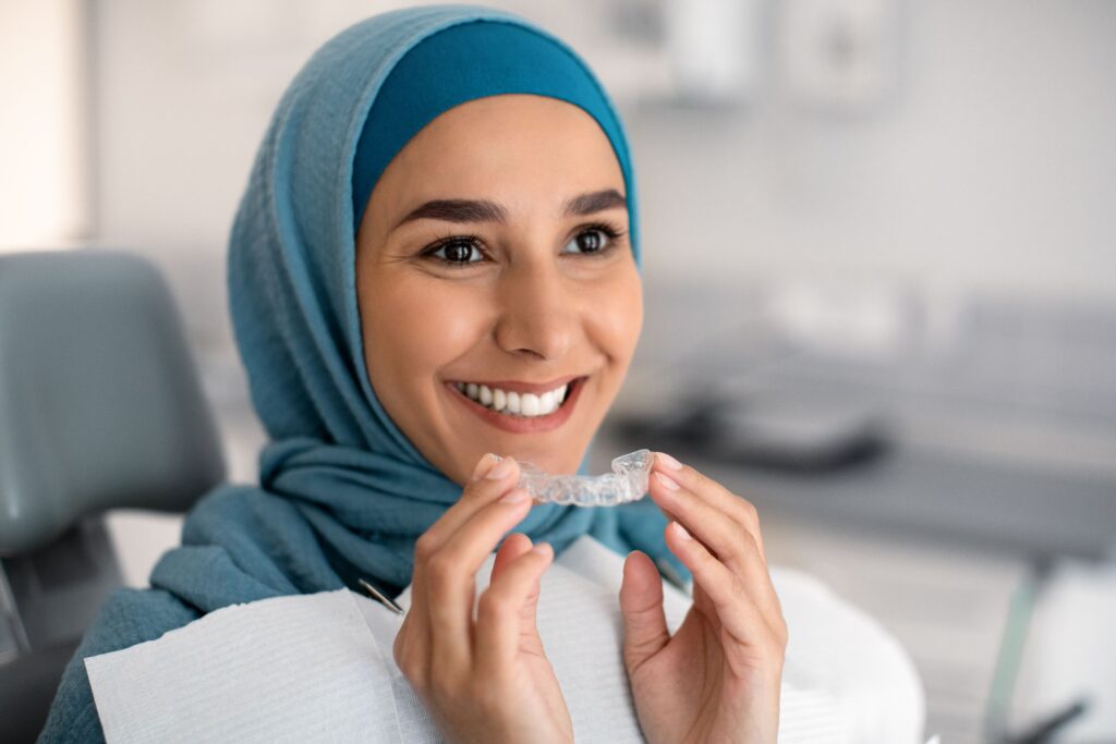 Woman in blue head covering in dental chair holding Invisalign