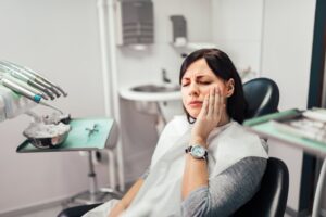 Woman holding jaw in pain in dentist's chair.